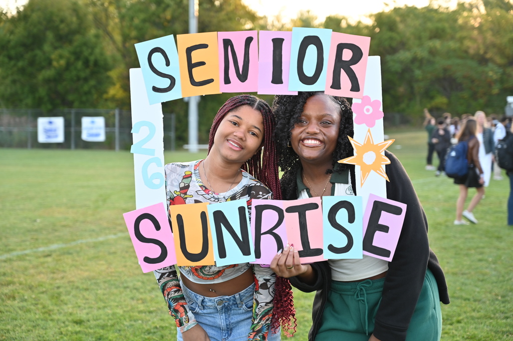 Two students pose behind a "Senior Sunrise" picture frame.