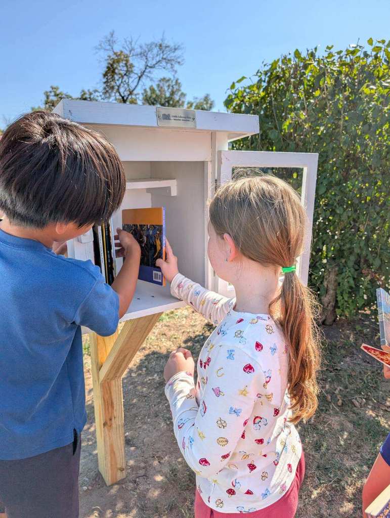 Two students place books in the Little Free Library.