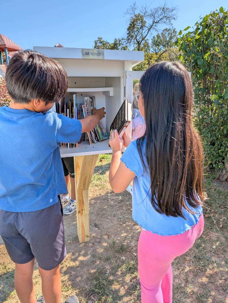 Two students place books in the Little Free Library.