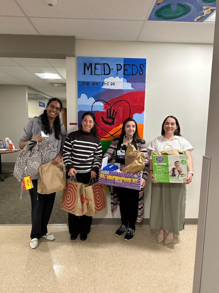 Four members of AMC hold bags and boxes of school supplies collected for donation to the North Colonie CSD.