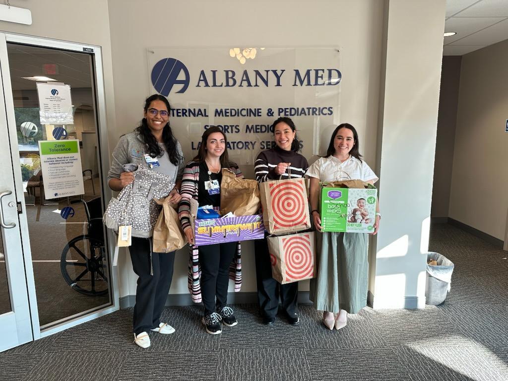 Four members of AMC hold bags and boxes of school supplies collected for donation to the North Colonie CSD.