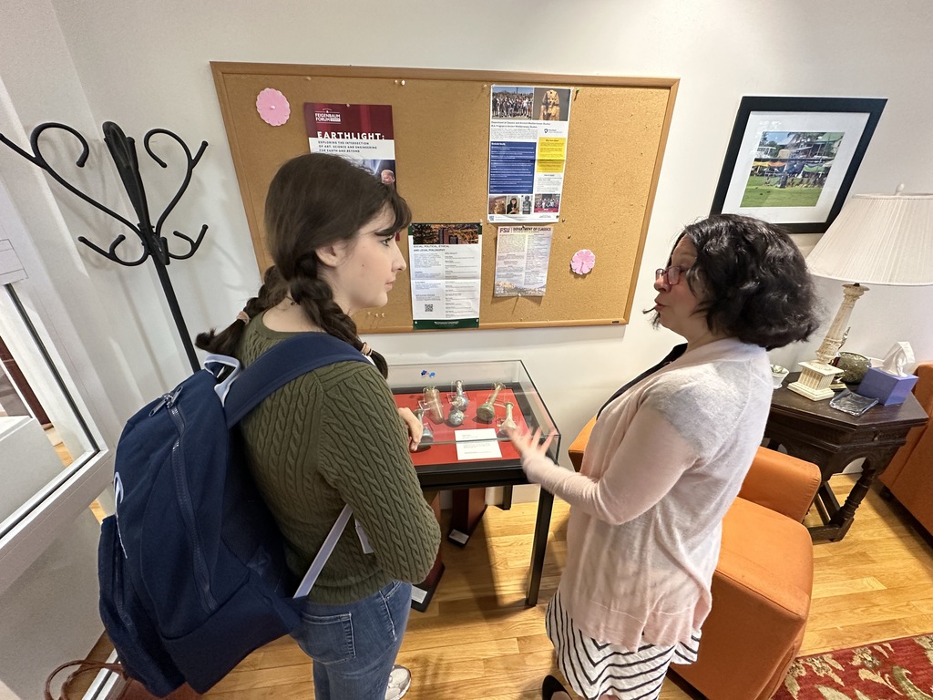 Dr. Stacie Raucci speaks to a student about the ancient artifacts encased in glass in front of them.