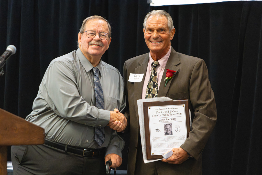 Shaker alum and former Athletic Director Dave Herman shakes hands as he holds his induction plaque.