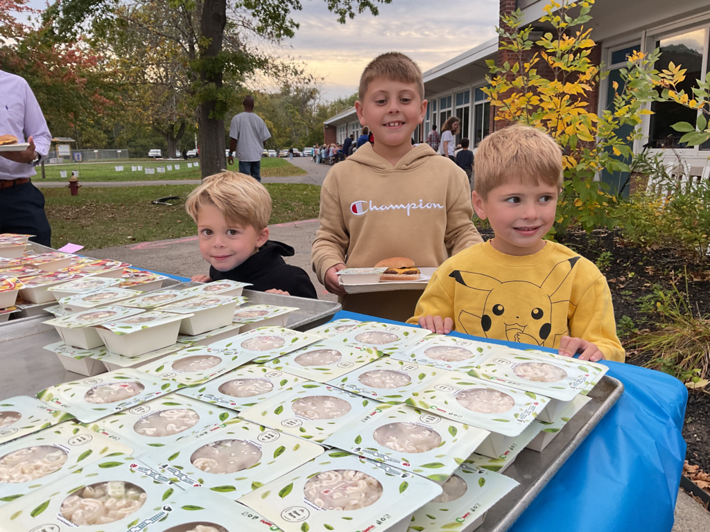 Three students stand behind a table with food on it.