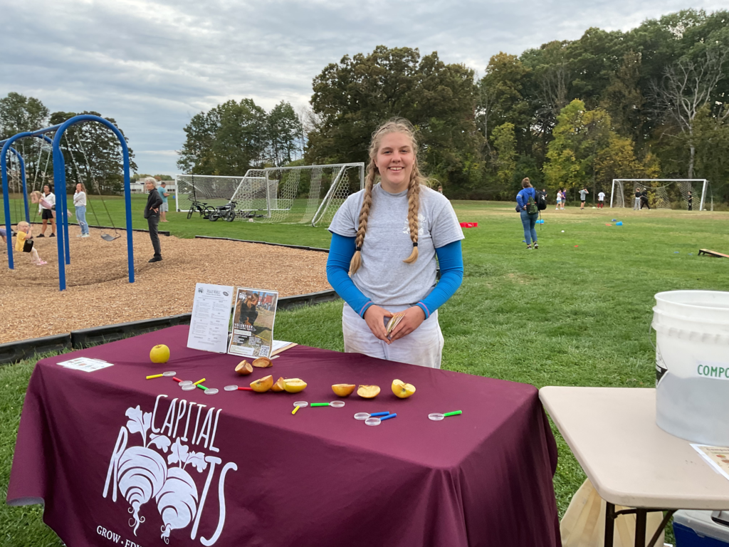 Someone from Capital Roots stands behind a table with apples on it.