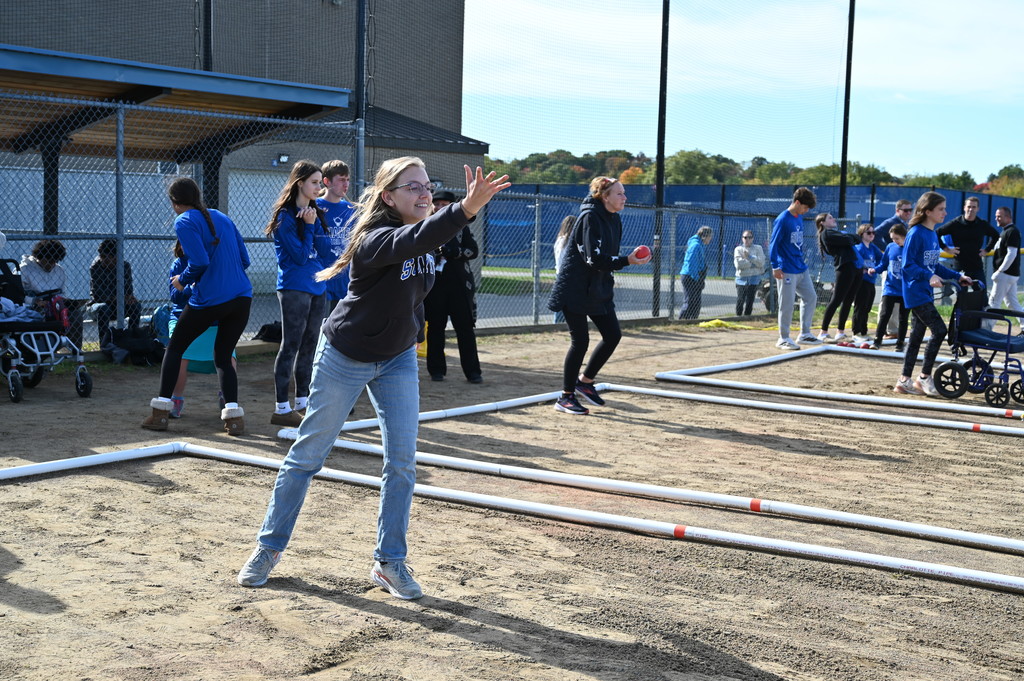 A faculty member lofts the bocce ball and watches it roll.