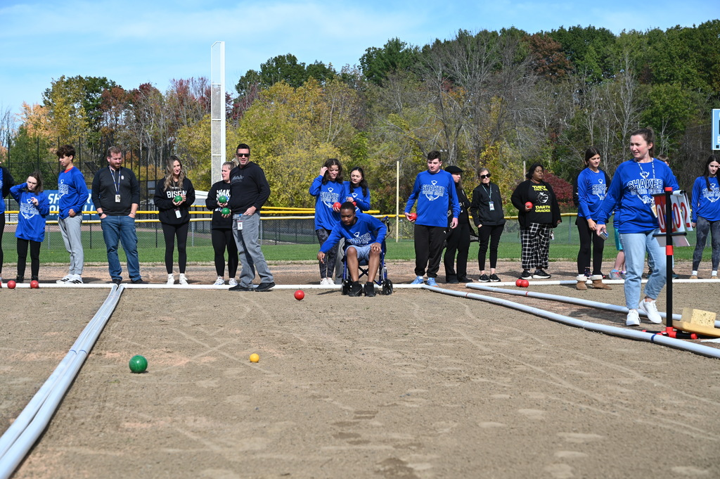 A student rolls a bocce ball from his wheelchair and watches it roll down the court.