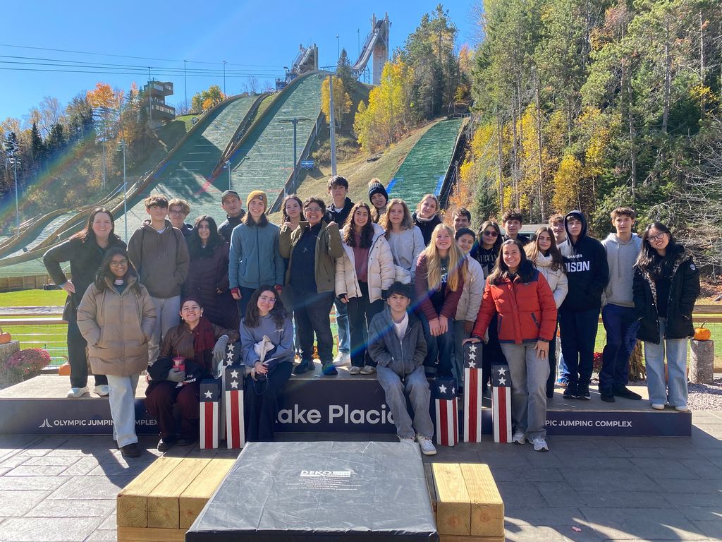A large group poses in front of the Olympic ski jumping venue in Lake Placid.