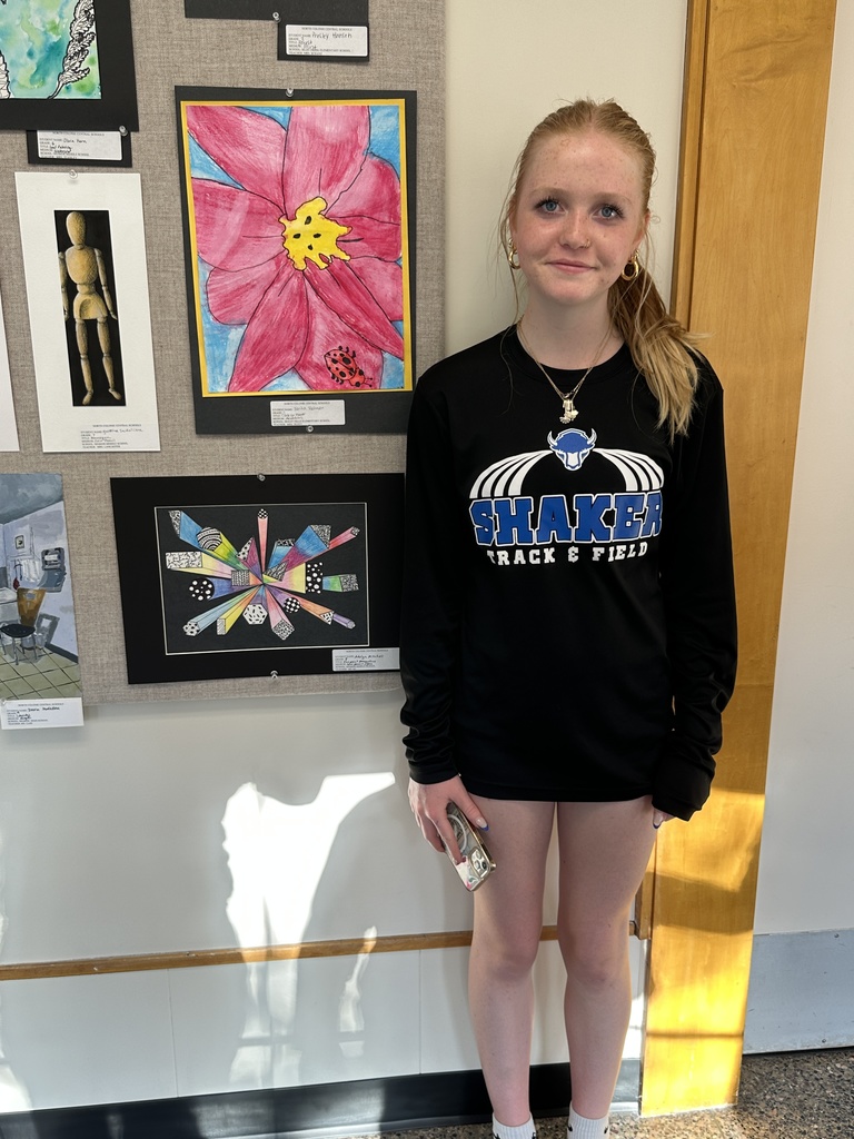 A student stands proudly next to her artwork on display.