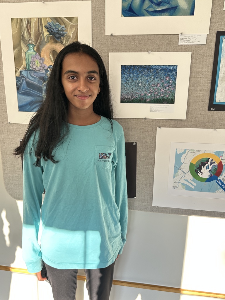 A student stands next to their artwork displayed in the Superintendent's gallery.