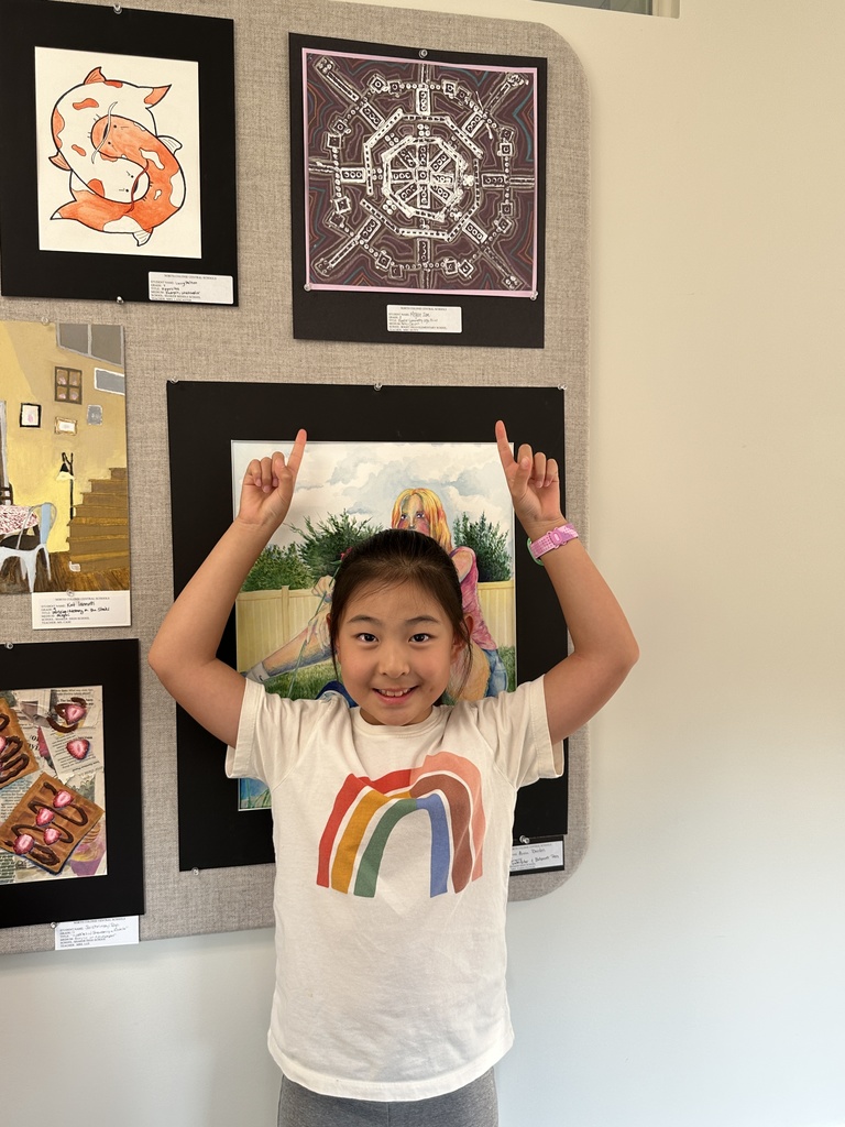 A student points to her artwork on display above her.