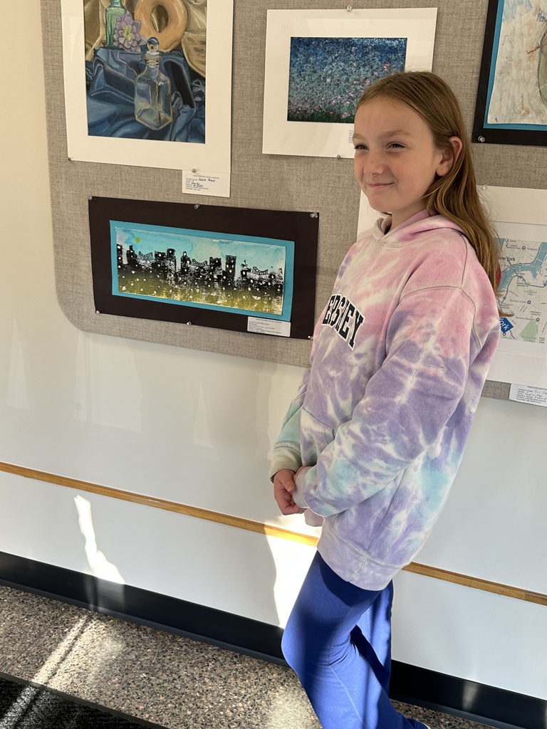 A student stands proudly next to her artwork on display.