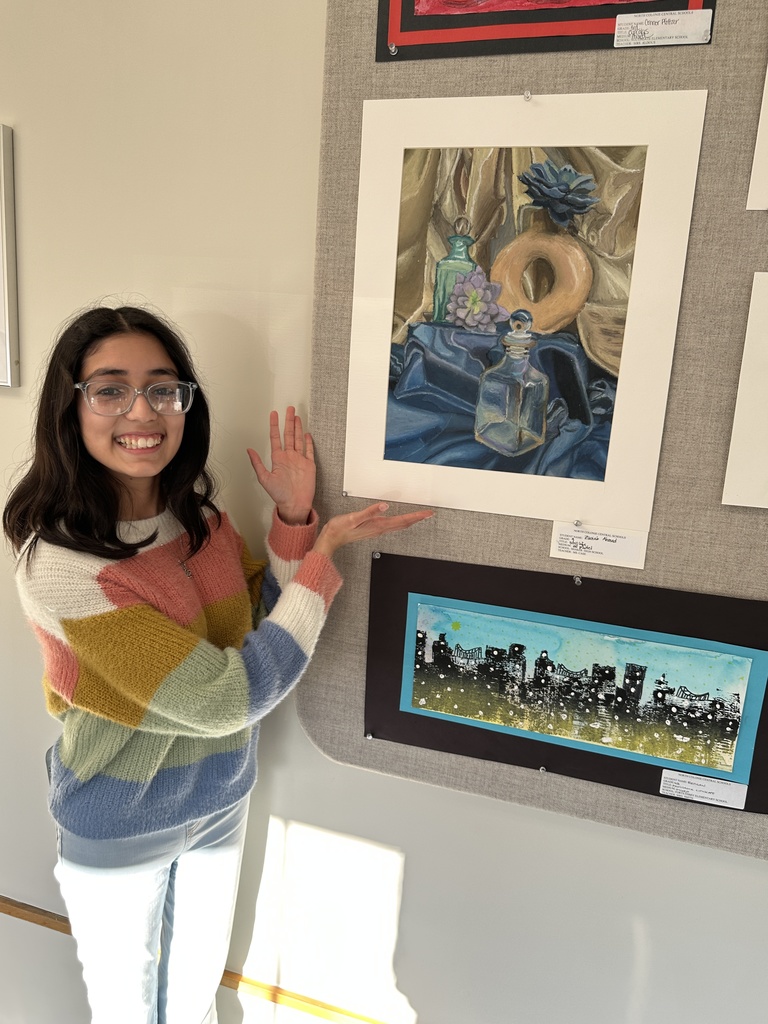 A students uses her hands to show off her artwork on display in the gallery.