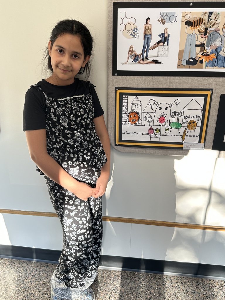 A student stands proudly next to her artwork on display.