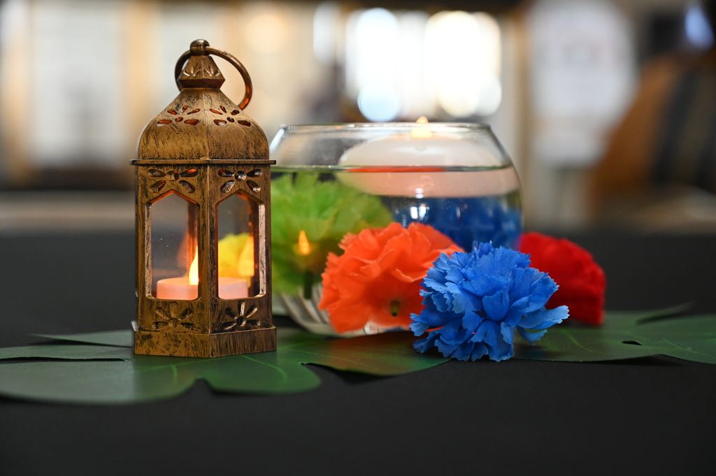 A table centerpiece which includes a lantern, candle and colorful flowers.