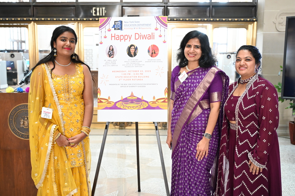 Shaker student Shubhika Garg stands next to an event poster alongside the emcee and keynote speaker.
