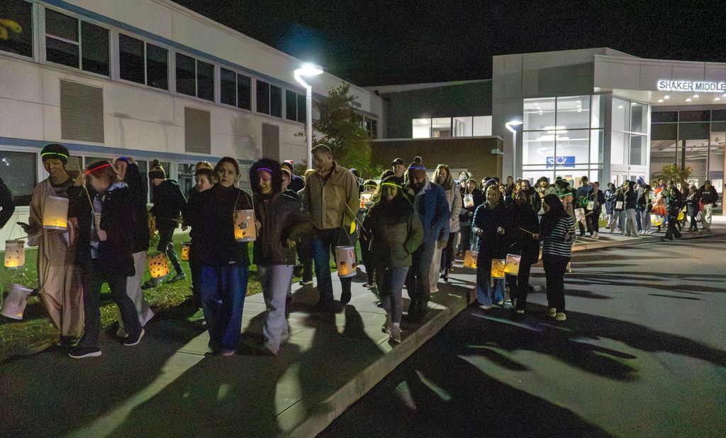 Hundreds of students and family members walk outside with glowing lanterns.