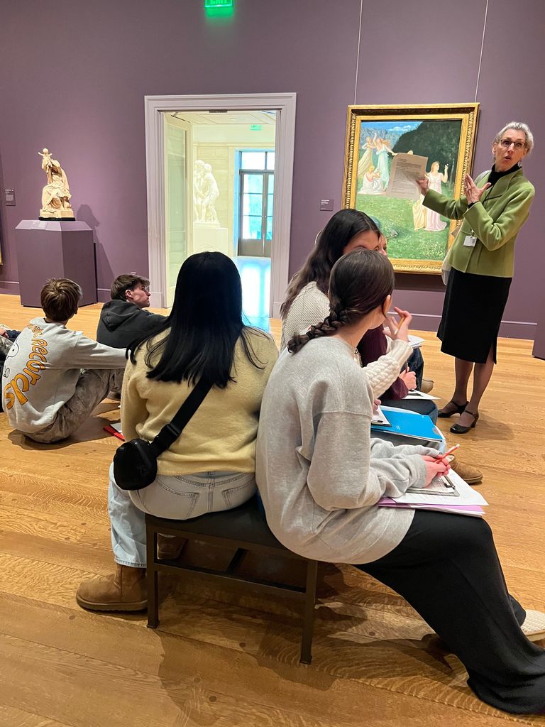 A member of the museum staff speaks to students who take notes.
