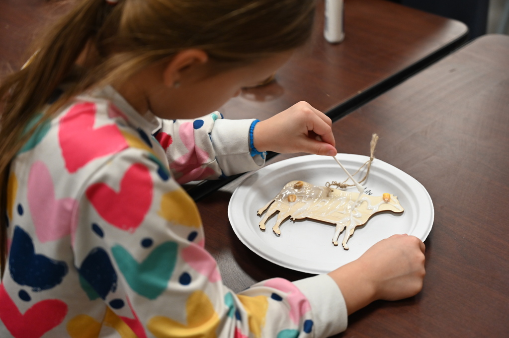 A student uses a q-tip to spread glue on a cut-out of a cow.