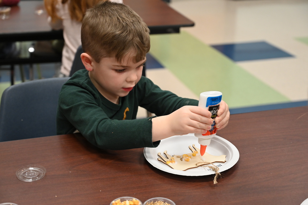 A student puts glue on a cut-out of a cow as part of a project.