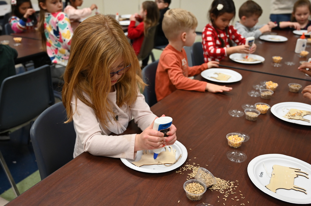 Students put glue on cut-outs of cows to decorate them.