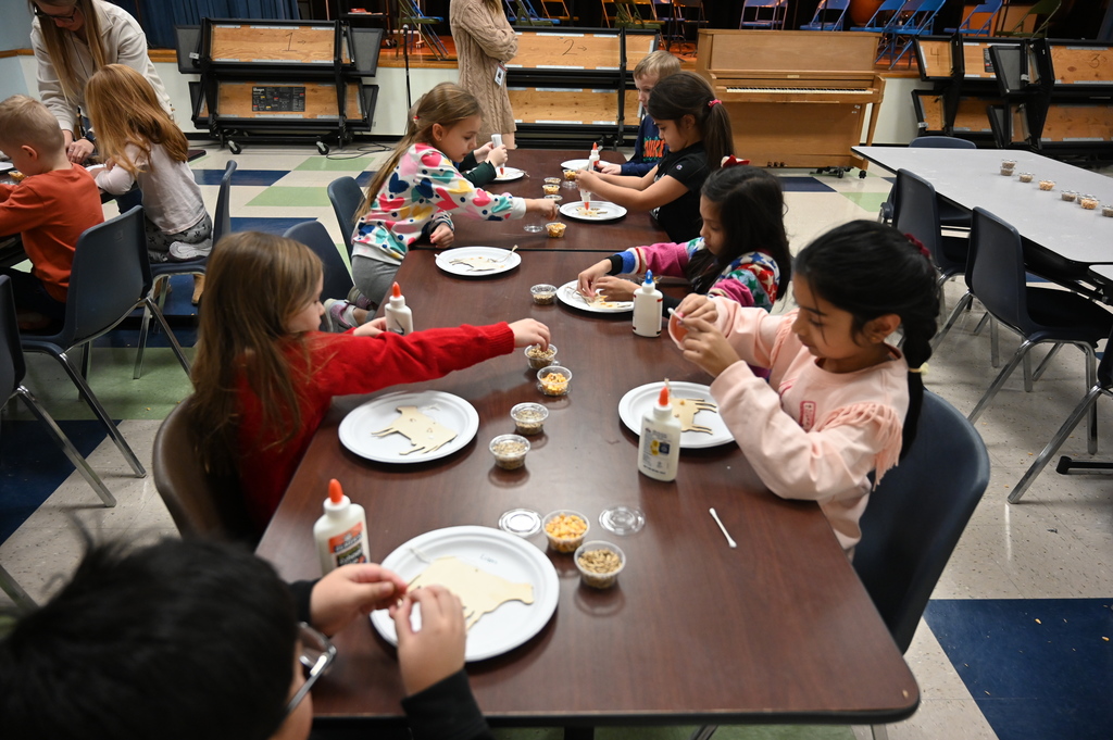 A group of students work to glue corn and grain to cut-outs of cows.