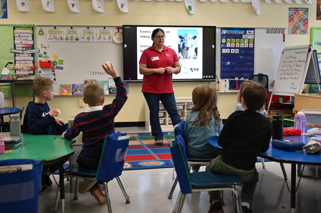 A representative from Cornell Cooperative Extension stands at the front of a room of students, presenting about cows.