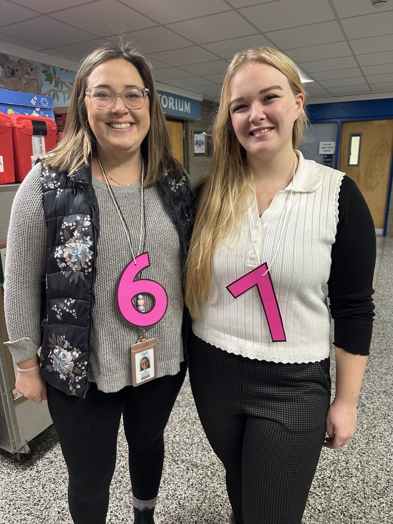 Two teachers wear a large pink "6" and "7" hanging around their neck to celebrate the 67th day of school.