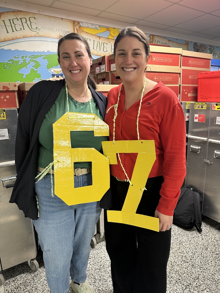 Two teachers wear a large yellow "6" and "7" hanging around their neck to celebrate the 67th day of school.