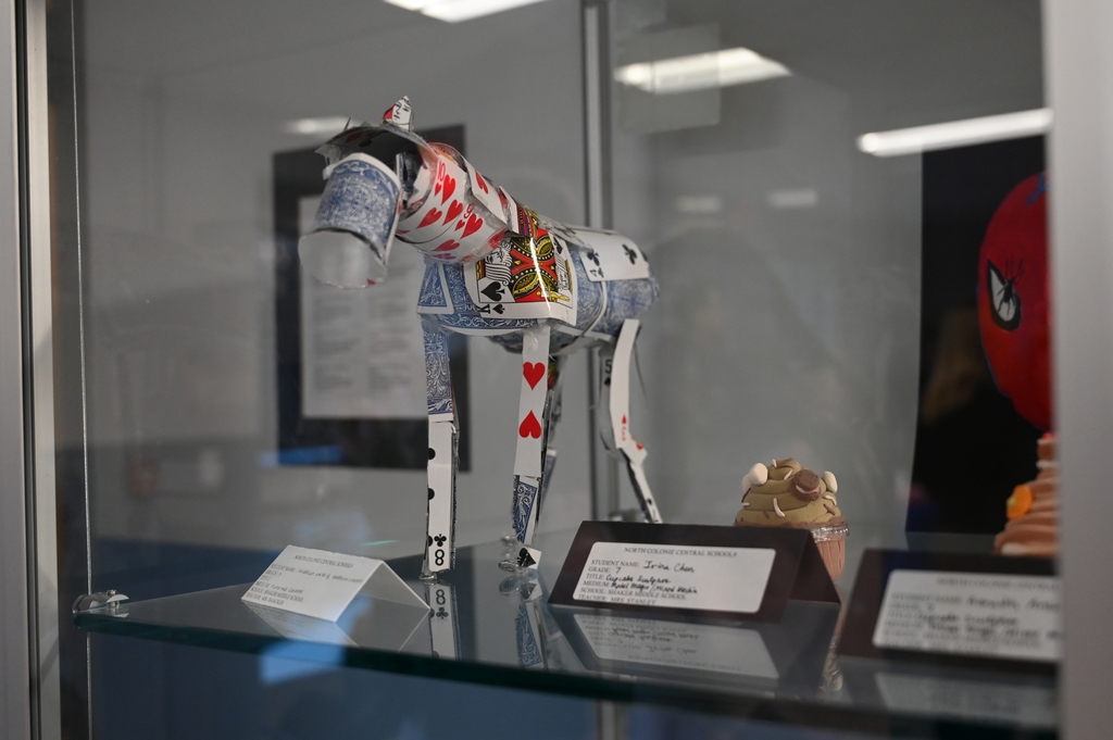 A horse made out of playing cards is displayed amongst other works in a glass case.