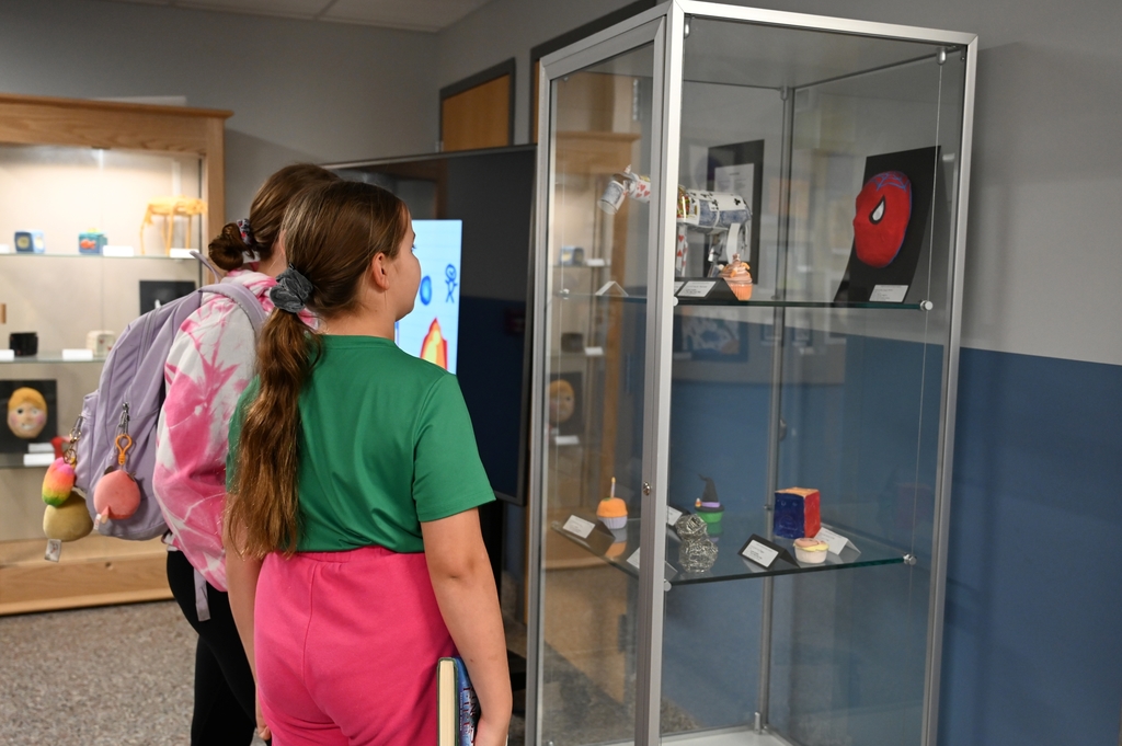 Two students look at artwork displayed in a glass case.