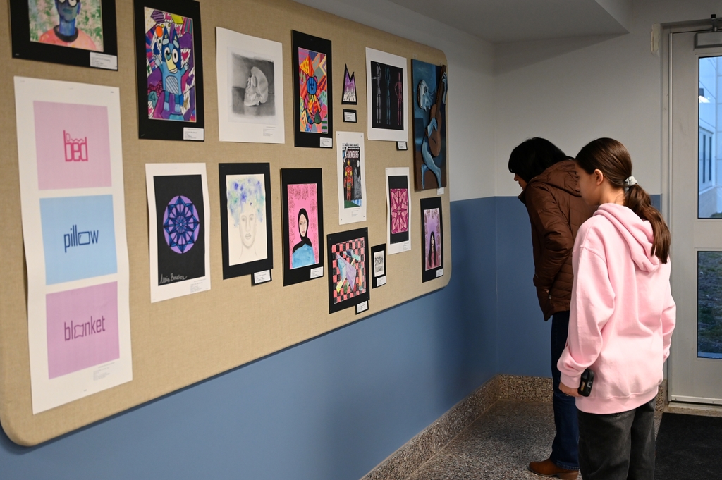 Two people look at artwork by Shaker Middle School students at a reception.