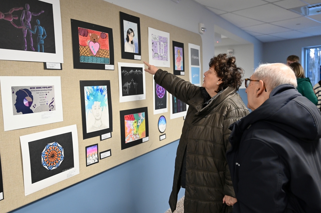 Two people enjoy works of art by Shaker Middle School students at a reception.