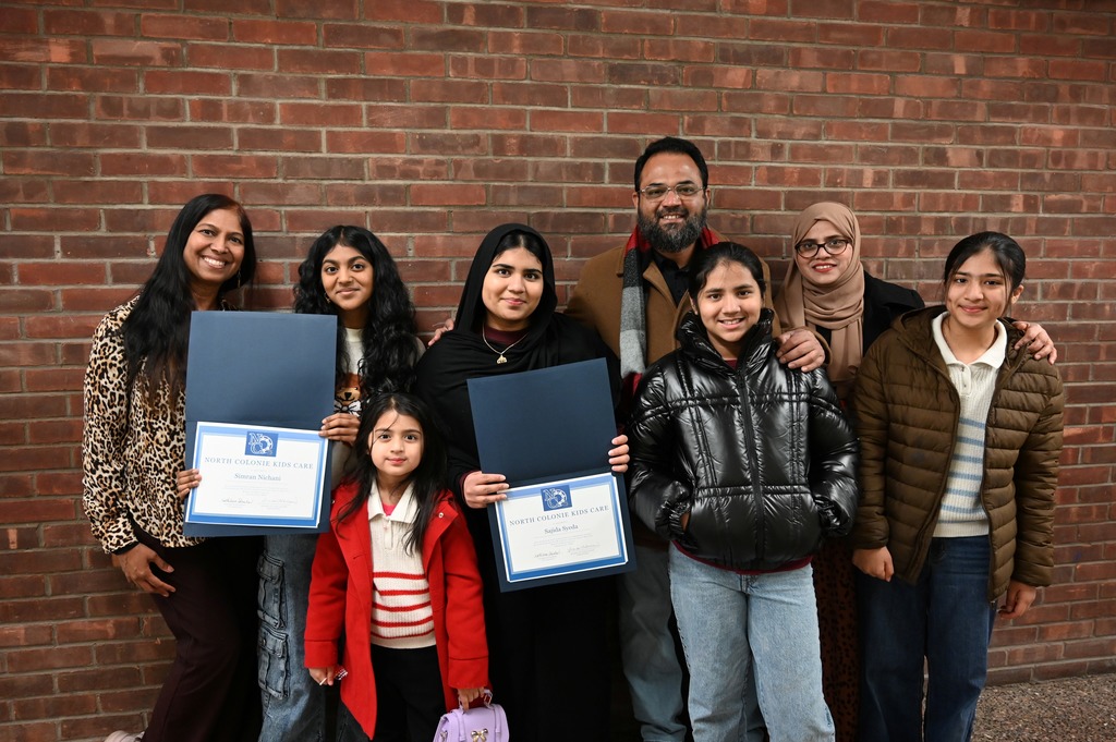 Two students and their families pose to celebrate their recognition as North Colonie Kids Care recipients.