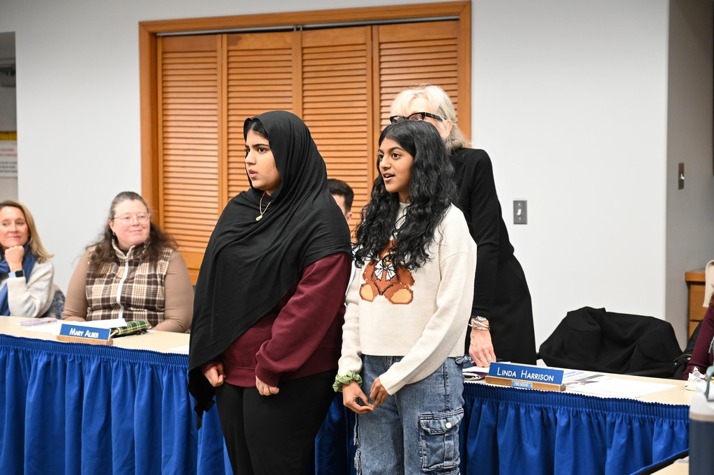 Two students stand at the front of a Board of Education meeting and speak about their work to start a Science Olympiad at Shaker Middle School.