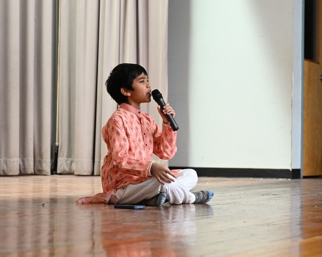 A student sings while seated on stage.
