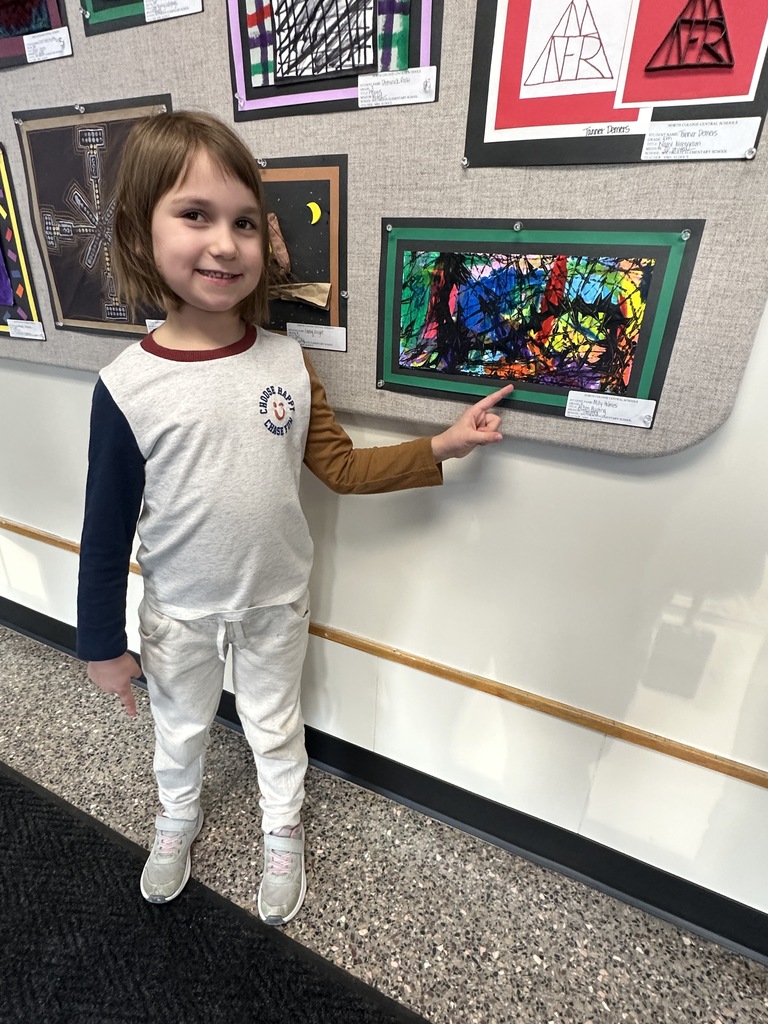 A student proudly points to her artwork on display.