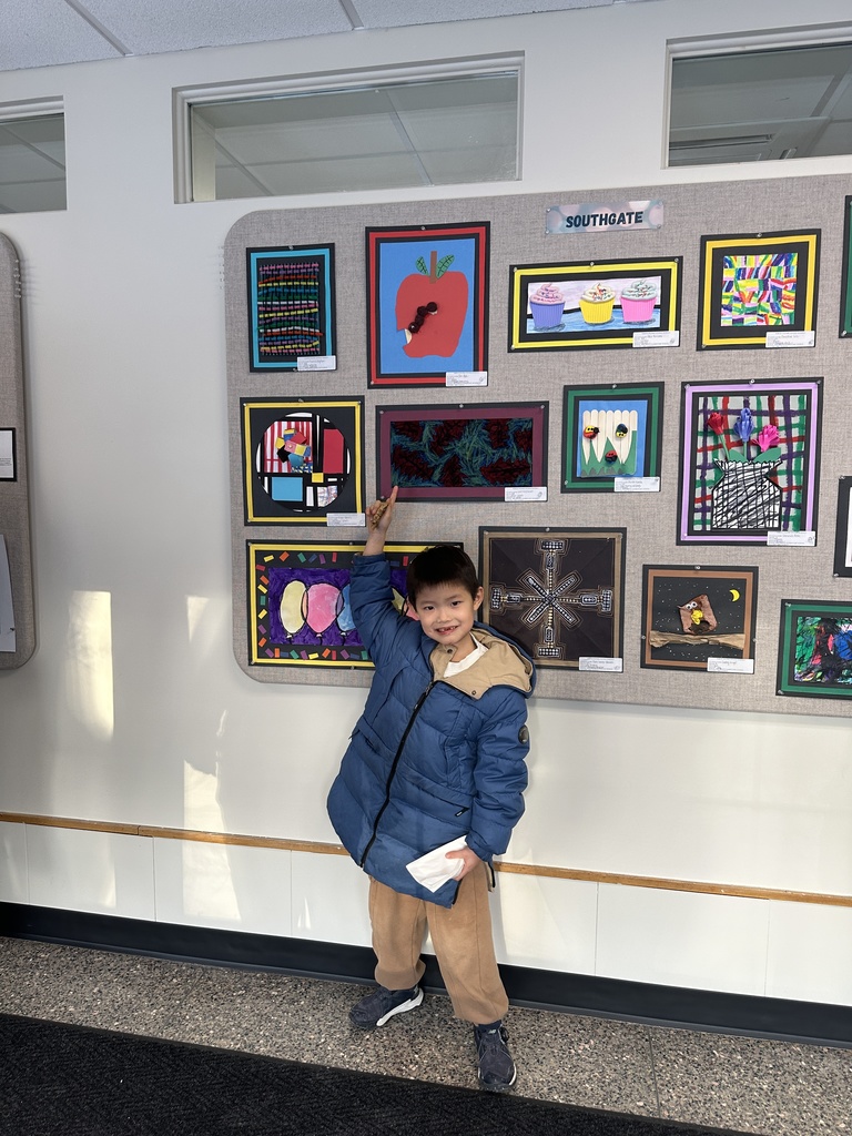 A student proudly points to his artwork on display above him.