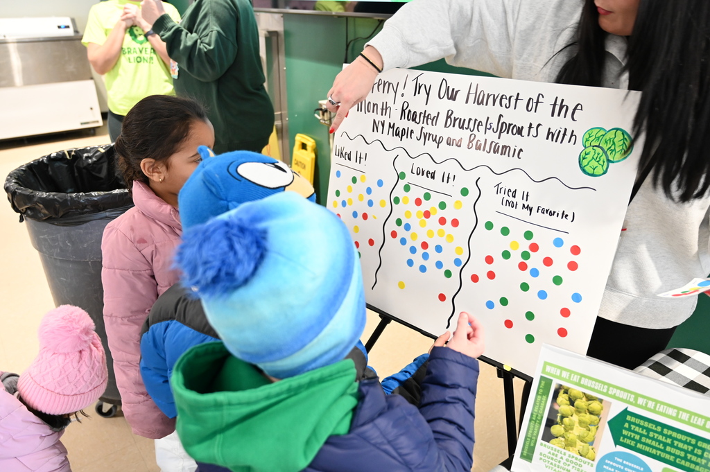 Students stand at a posterboard and decide where to put their stickers.