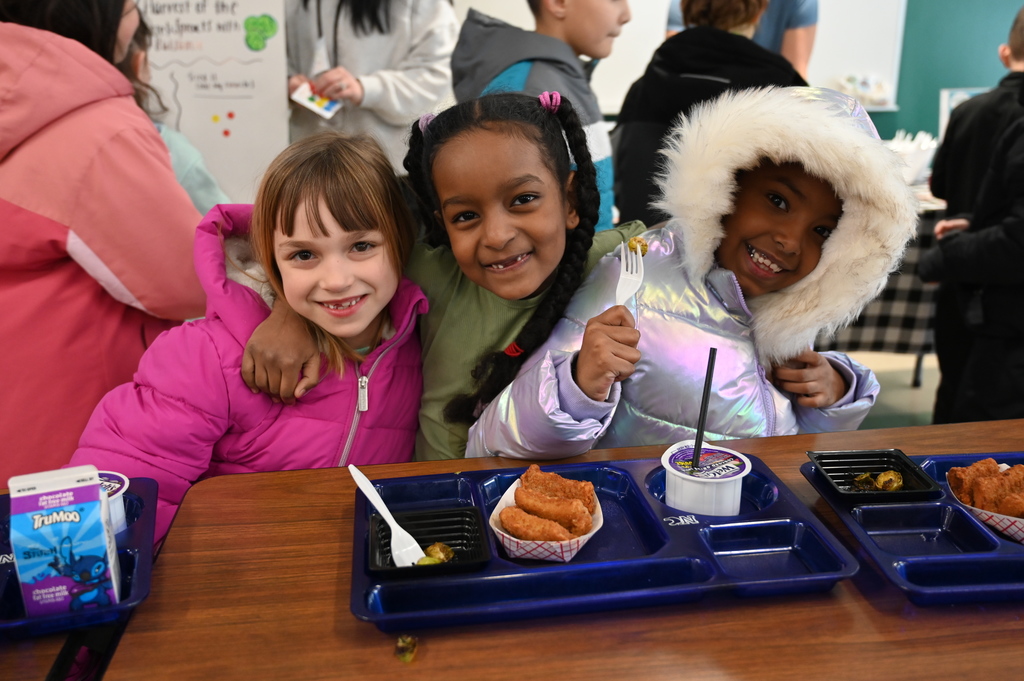 Three students pose together at a lunch table with food in front of them.