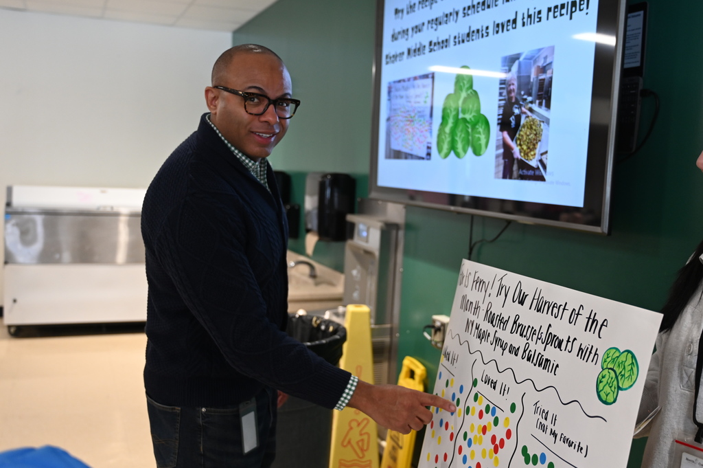 Dr. Parker places a sticker under the "Liked It" category on the Harvest of the Month posterboard.