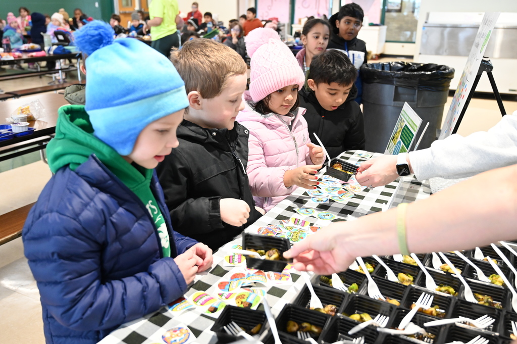Students take samples of Brussels sprouts from a table at the front of the cafeteria.