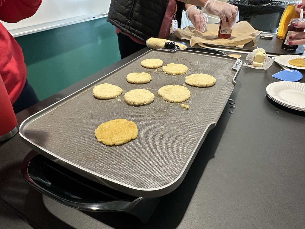Eight johnnycakes cook on a table top griddle.