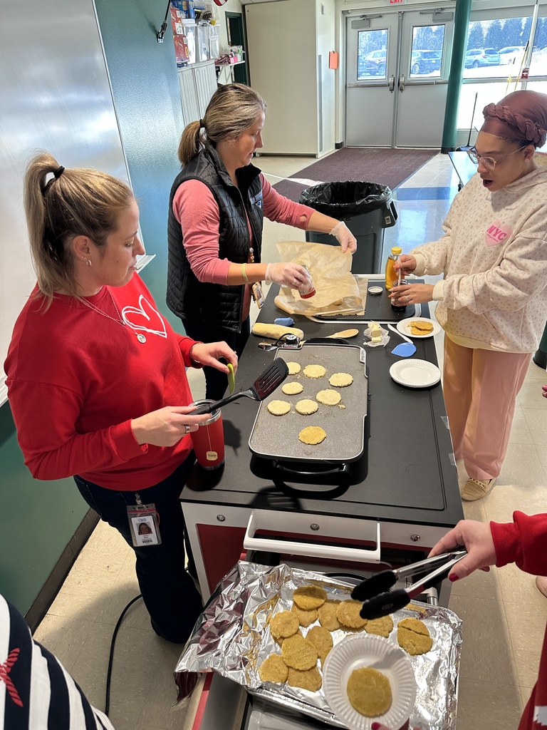 Two staff members cook up johnnycakes for other staff members on a griddle.