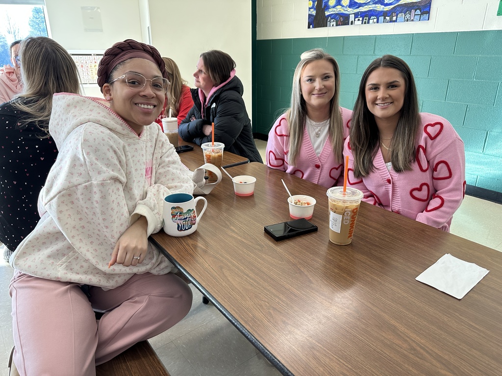 Three staff members pose in their Valentine's Day clothing as they sit at a table.