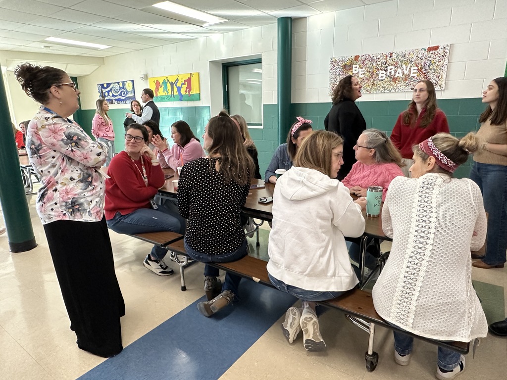 Superintendent Kathleen Skeals stands and talks to staff members who are seated at cafeteria tables.