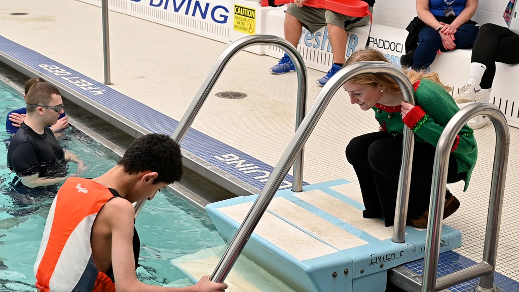 Evie encourages Haitham from outside the pool as he goes down the pool steps.