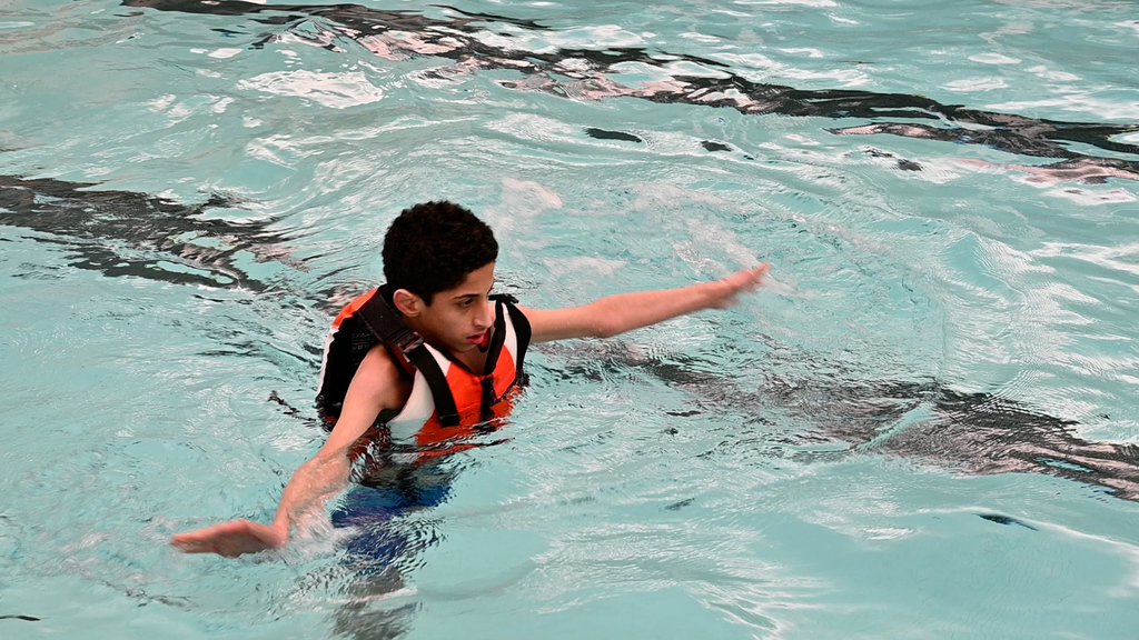 A student in a life jacket walks around the pool confidently.