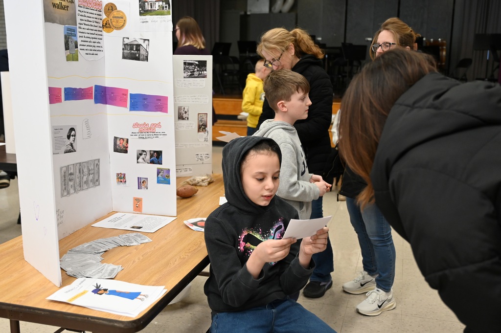 A student sits and reads a presentation to a visiting parent.