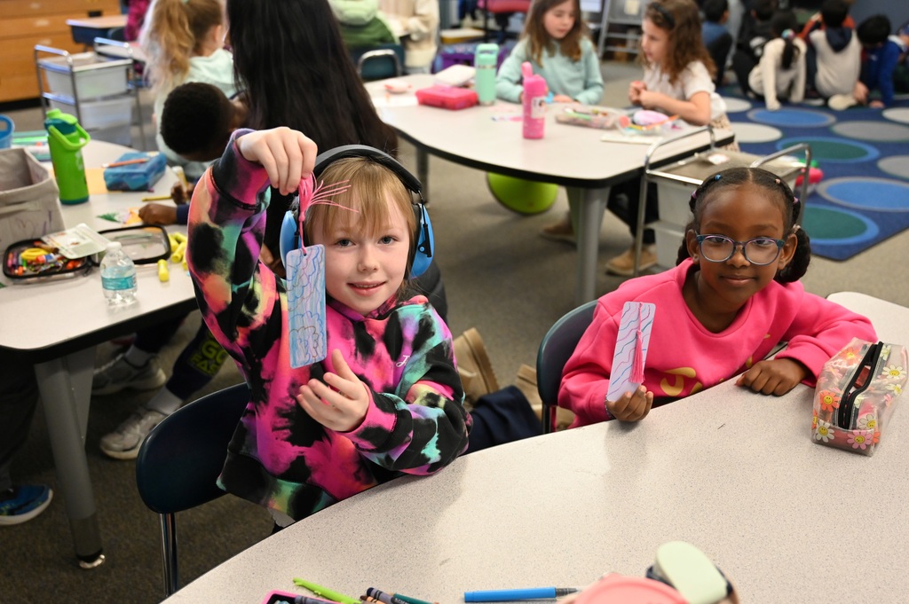 Two students show off their handmade bookmarks as they sit at a table.